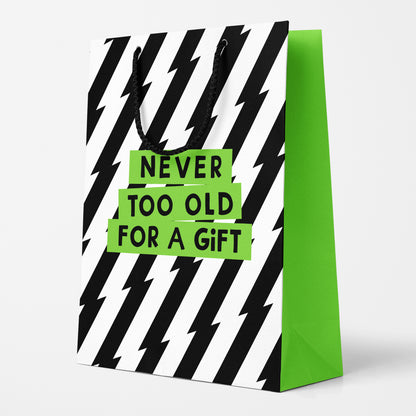 Birthday gift bag with black and white lightning stripe pattern and lime green blocks that say ‘Never Too Old for a Gift.’ Side panel reads ‘Pssst… never too old for cake